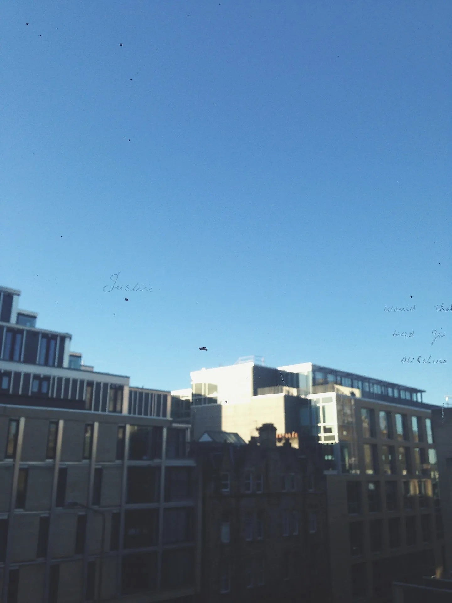 View of buildings from a window with some words scratched onto the glass.