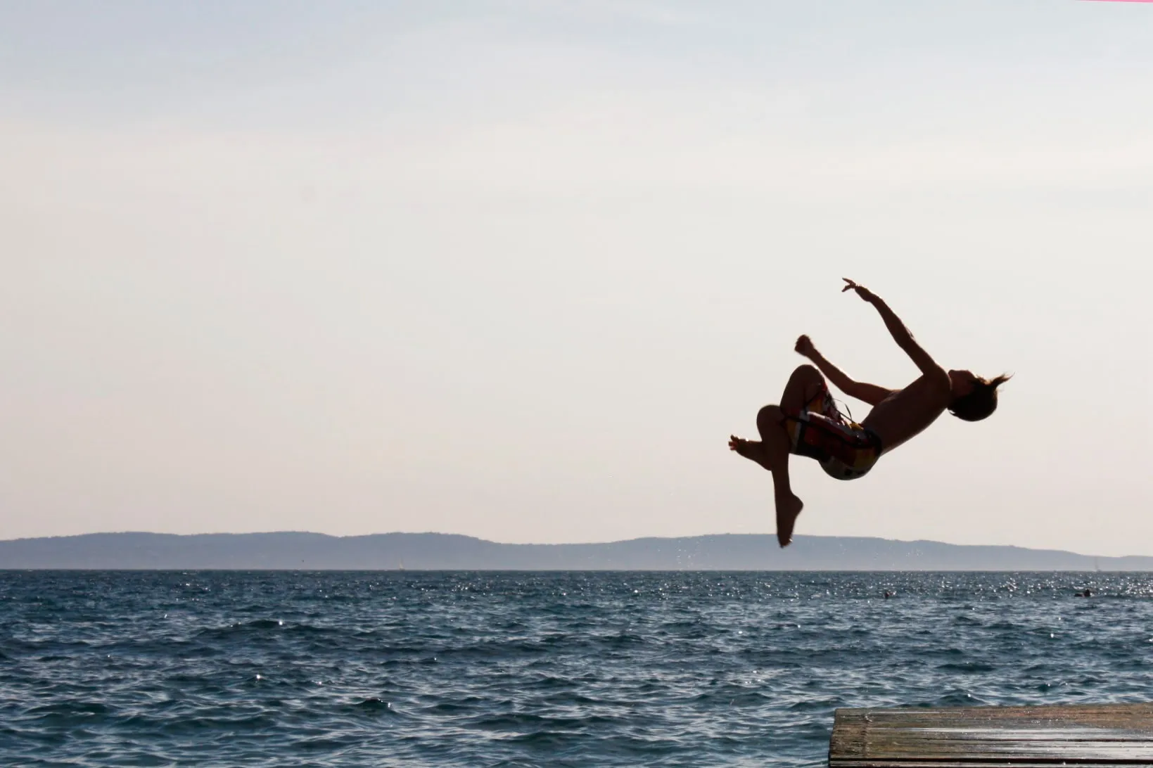 A kid in the middle of a salto, jumping into the sea.